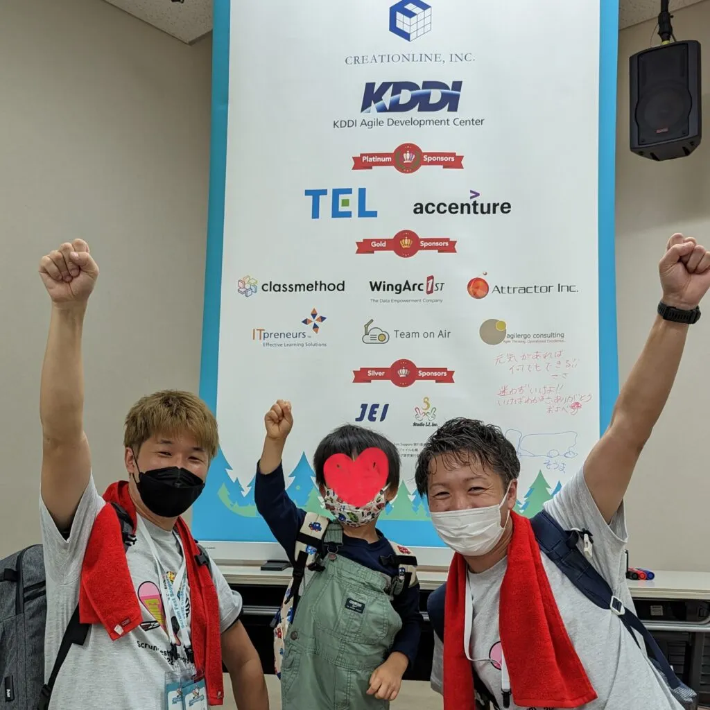 登壇後にスポンサーバナーの前でガッツポーズする3人