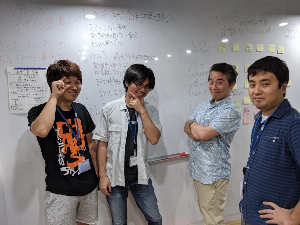 ホワイトボードの前に並ぶチームメンバー4人の記念写真
